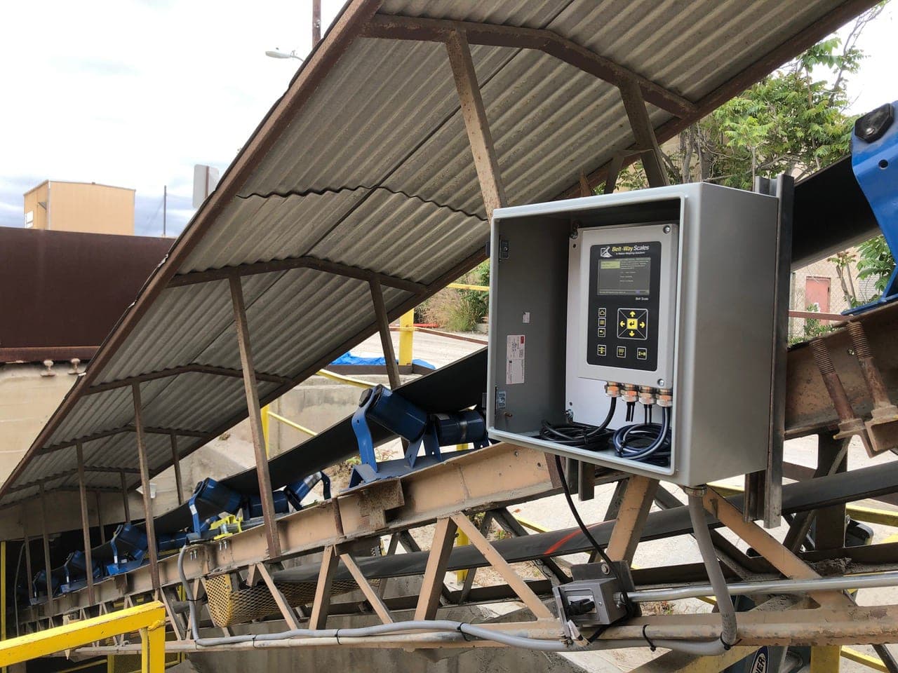 Belt scale integrator in a weatherproof enclosure beside a plant conveyor